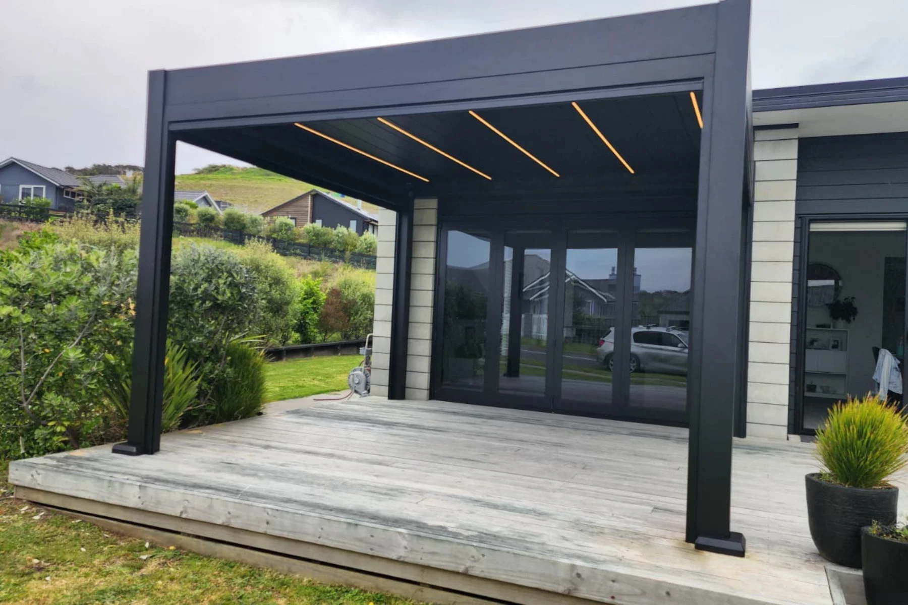 Pergola auf Holzterrasse, vor einem Haus.